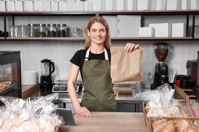 Photo of Happy seller with paper bag at cashier desk in bakery shop