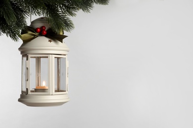 Photo of Vintage Christmas lantern with burning candle hanging on fir branch against light background. Space for text