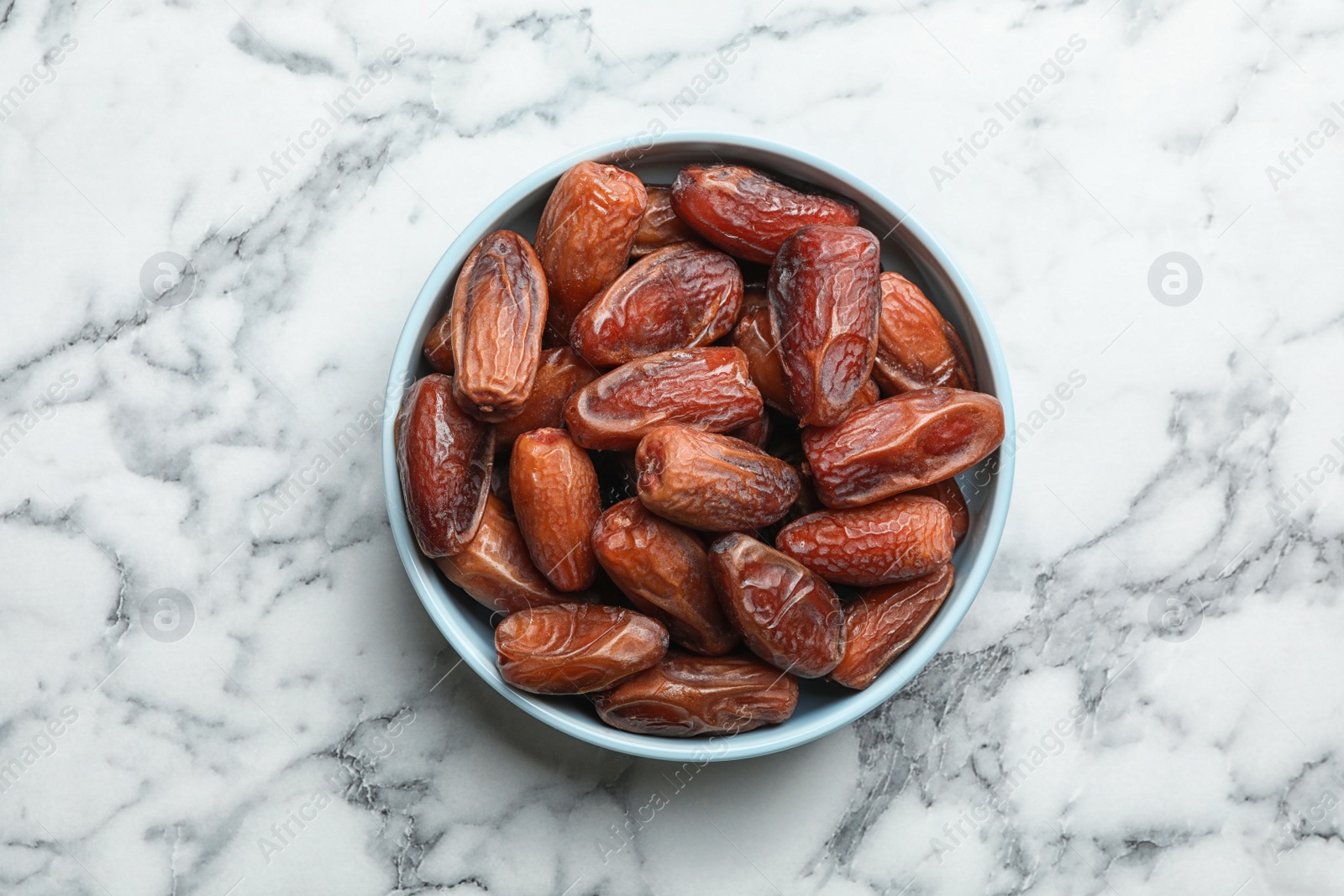 Photo of Bowl with sweet dried date fruits on marble background, top view