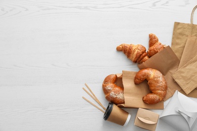 Photo of Flat lay composition with paper bags and pastry on light wooden background. Space for design