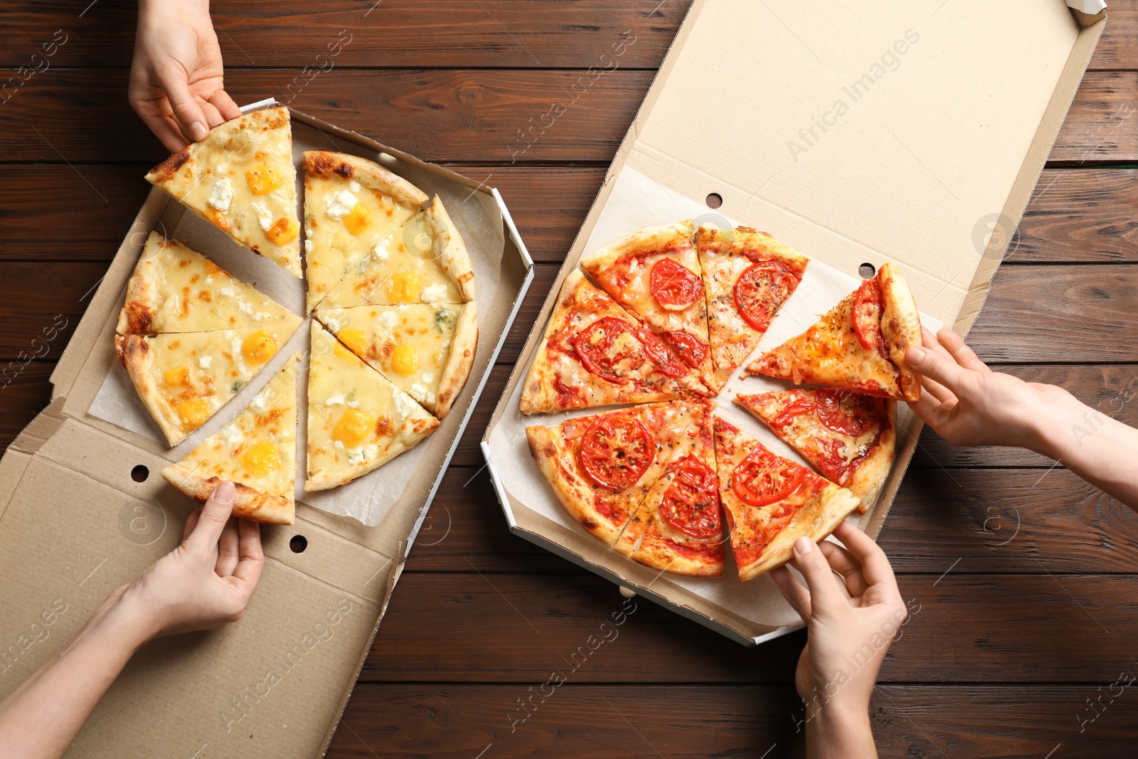 Photo of Young people taking slices of hot cheese pizzas from cardboard boxes at table, top view. Food delivery service