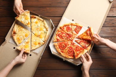 Photo of Young people taking slices of hot cheese pizzas from cardboard boxes at table, top view. Food delivery service