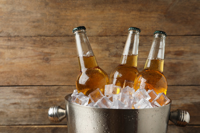 Photo of Metal bucket with beer and ice cubes on wooden background