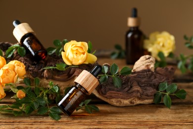 Bottles of rose essential oil and flowers on wooden table