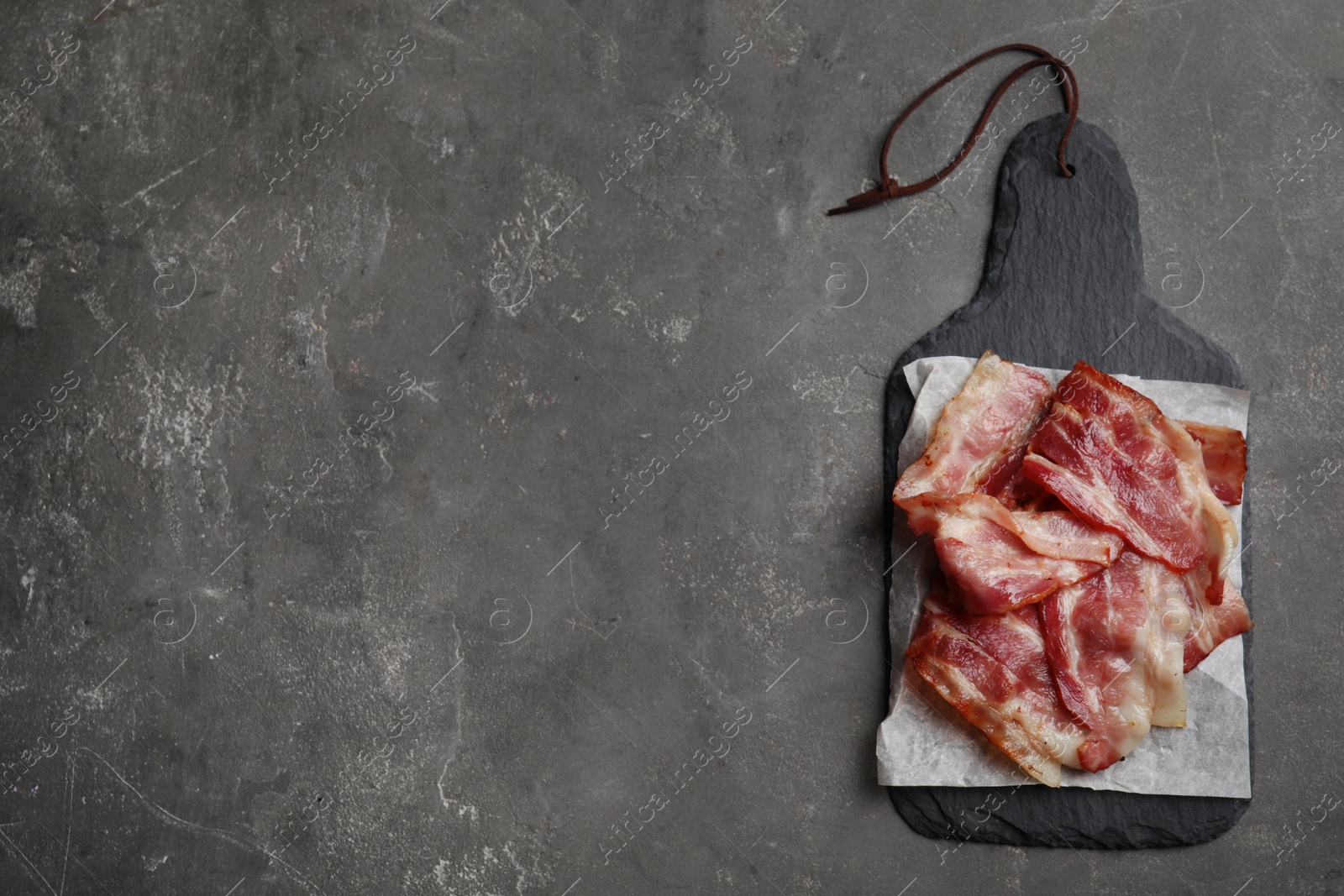 Photo of Slices of tasty fried bacon on grey table, top view. Space for text