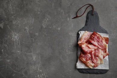 Photo of Slices of tasty fried bacon on grey table, top view. Space for text