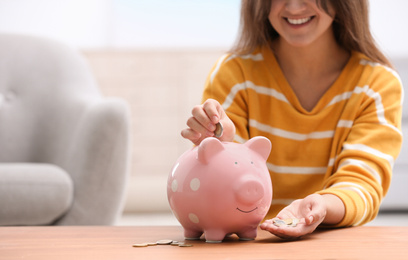 Photo of Woman putting coin into piggy bank at wooden table, closeup. Space for text
