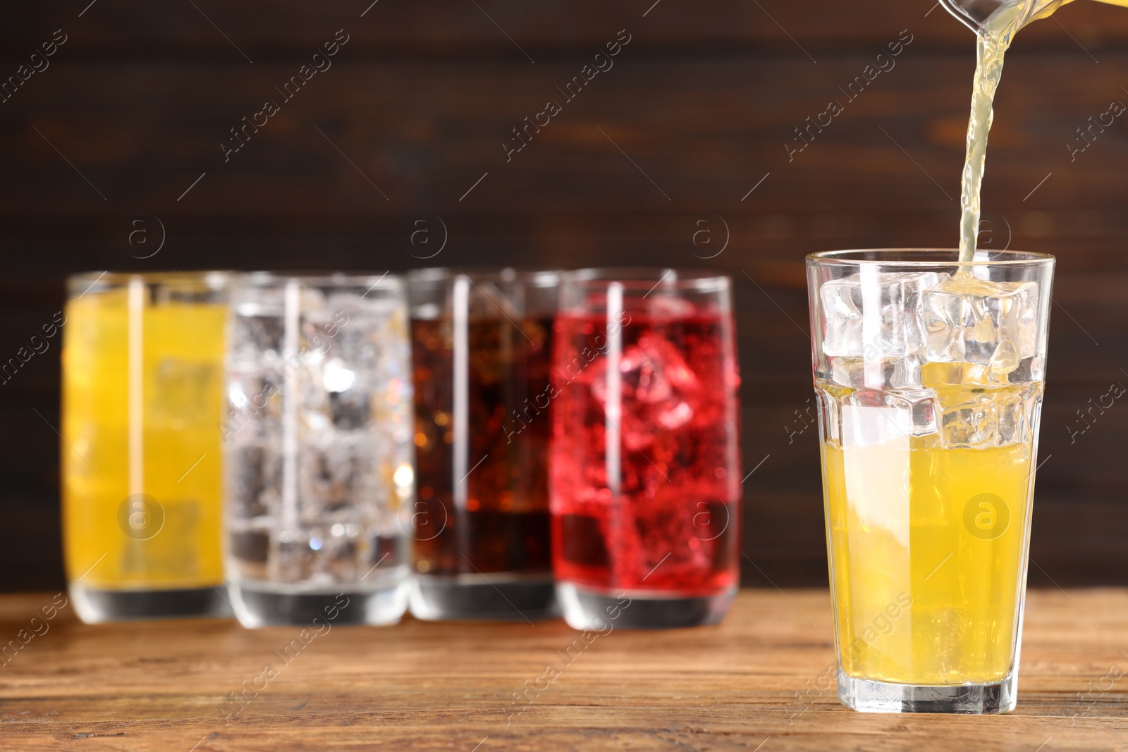 Photo of Pouring refreshing soda water in glass with ice cubes on wooden table, space for text