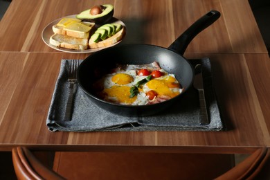 Fried eggs with bacon and tomatoes served with toasts on wooden table. Tasty breakfast