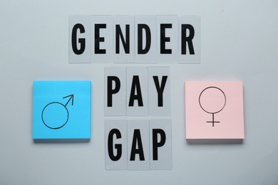 Photo of Gender pay gap. Paper notes with male and female symbols on grey background, flat lay
