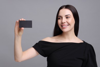 Happy woman holding blank business card on grey background