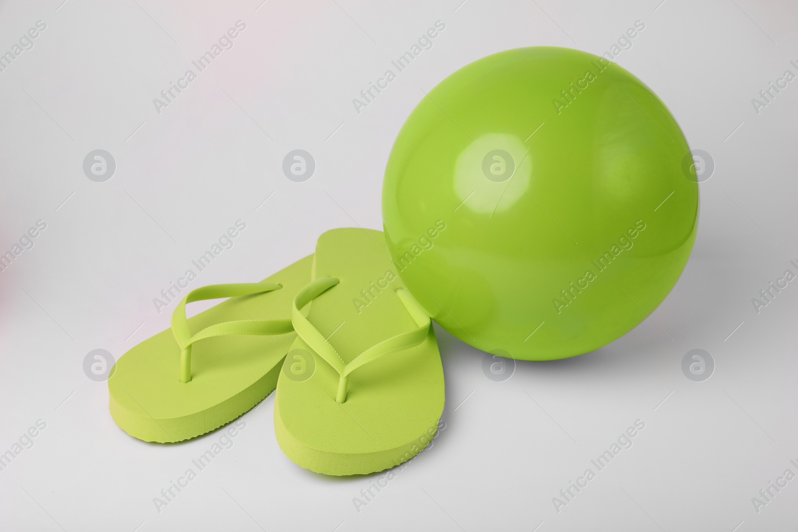 Photo of Green inflatable beach ball and flip flops on white background