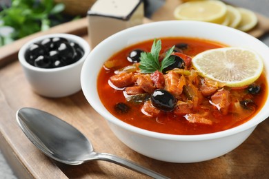 Photo of Meat solyanka soup with sausages, olives, vegetables in bowl and spoon on grey table, closeup