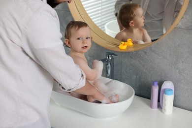 Father washing his little baby in sink at home