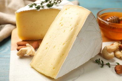 Photo of Tasty Camembert cheese with thyme, honey and nuts on light blue wooden table, closeup