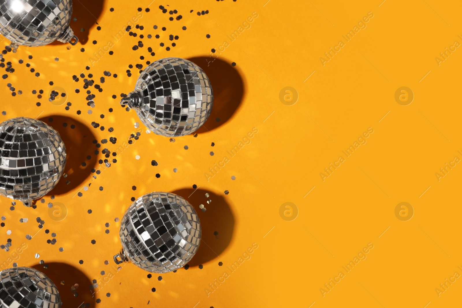 Photo of Bright shiny disco balls and confetti on orange background, flat lay. Space for text