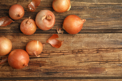 Many ripe onion bulbs on wooden table, flat lay. Space for text