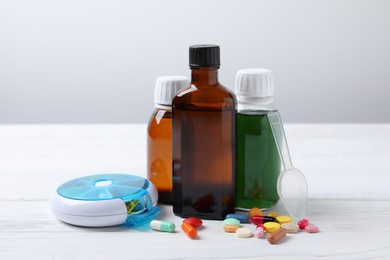 Photo of Bottles of syrup, dosing spoon and pills on white table against light grey background. Cold medicine