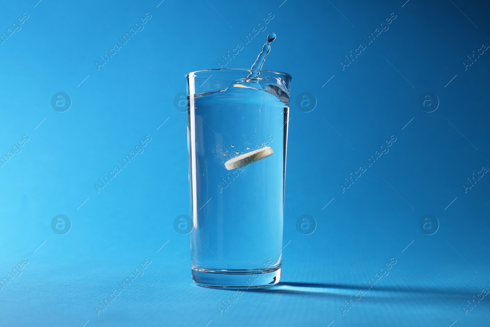 Photo of Effervescent pill dissolving in glass of water on light blue background