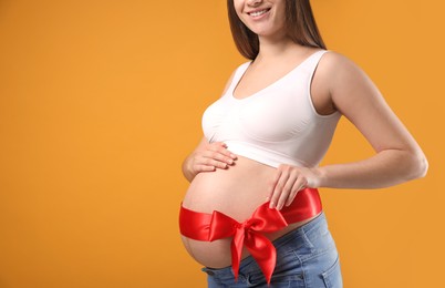Photo of Young pregnant woman with red bow on her belly against yellow background, closeup and space for text. Time to give birth
