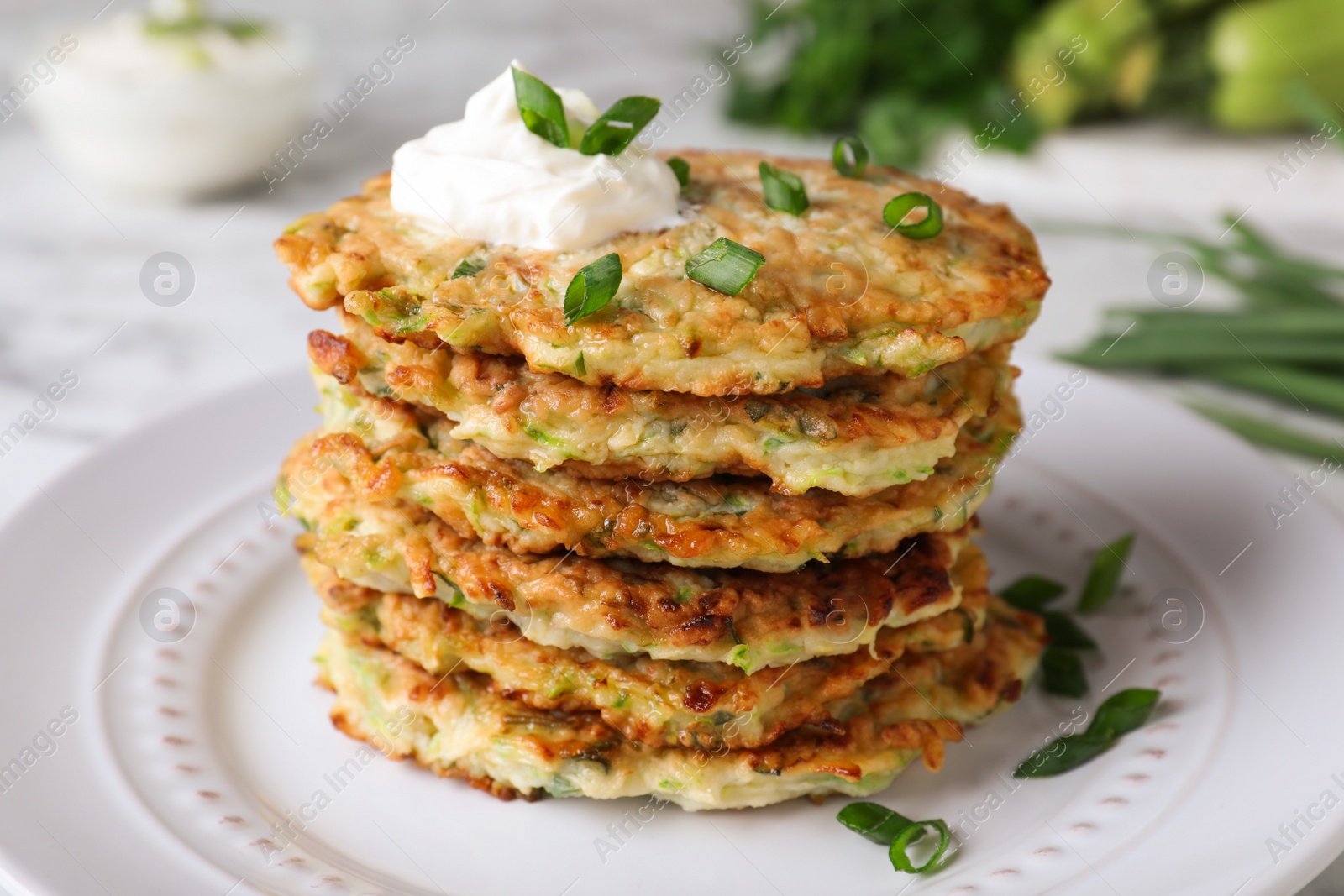 Photo of Delicious zucchini fritters with sour cream and green onion on plate, closeup