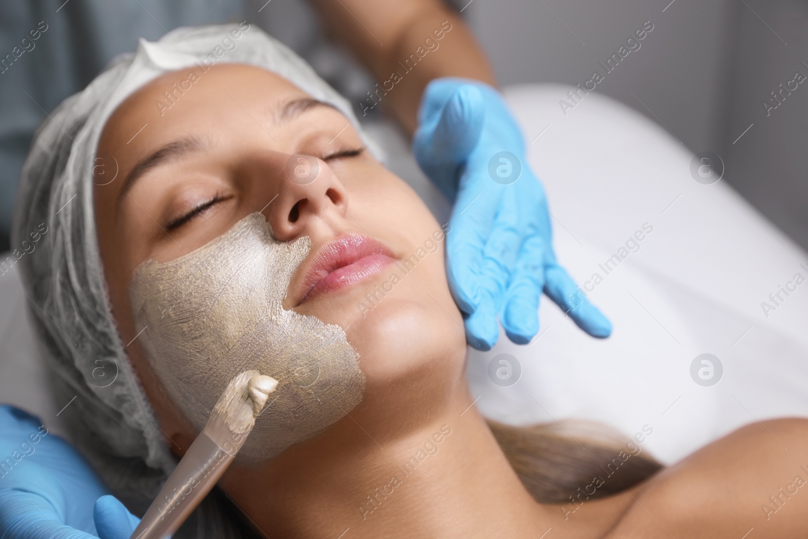 Photo of Cosmetologist applying mask on client's face in spa salon