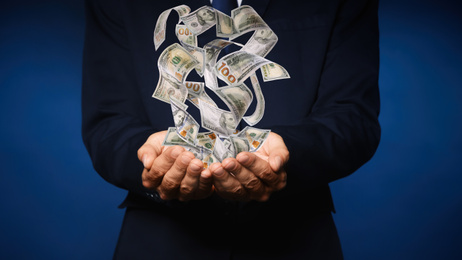 Image of Businessman with money on dark blue background, closeup. Currency exchange