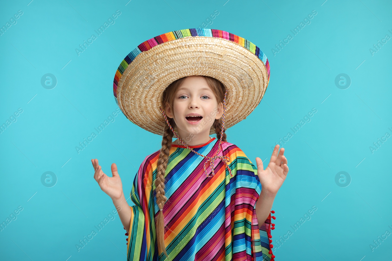 Photo of Surprised girl in Mexican sombrero hat and poncho on light blue background