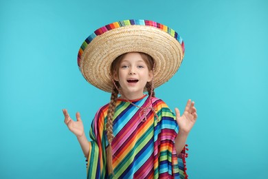 Surprised girl in Mexican sombrero hat and poncho on light blue background