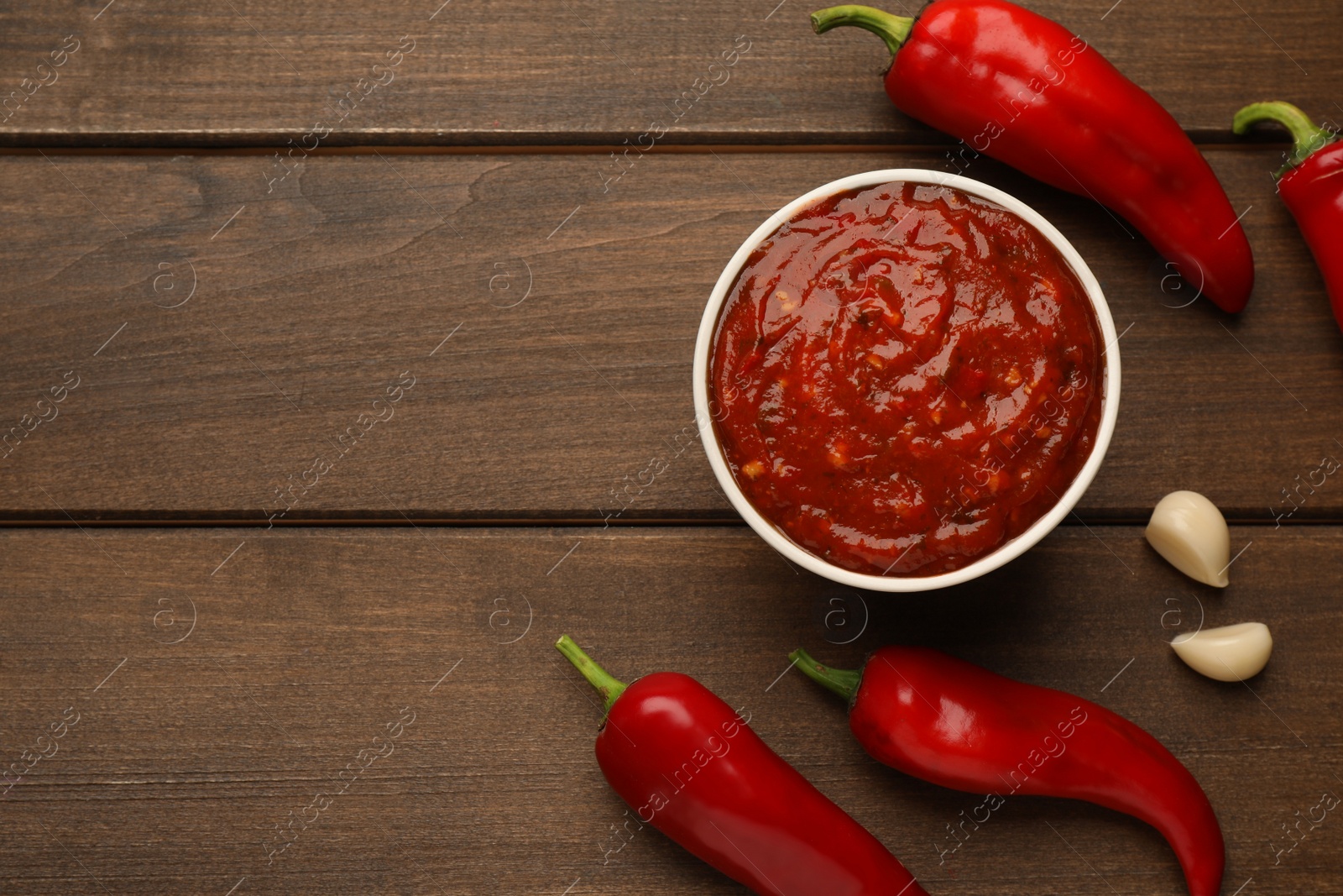 Photo of Delicious adjika sauce in bowl and ingredients on wooden table, flat lay. Space for text