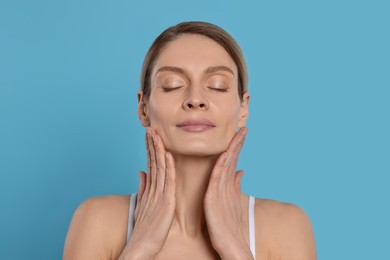 Photo of Woman massaging her face on turquoise background