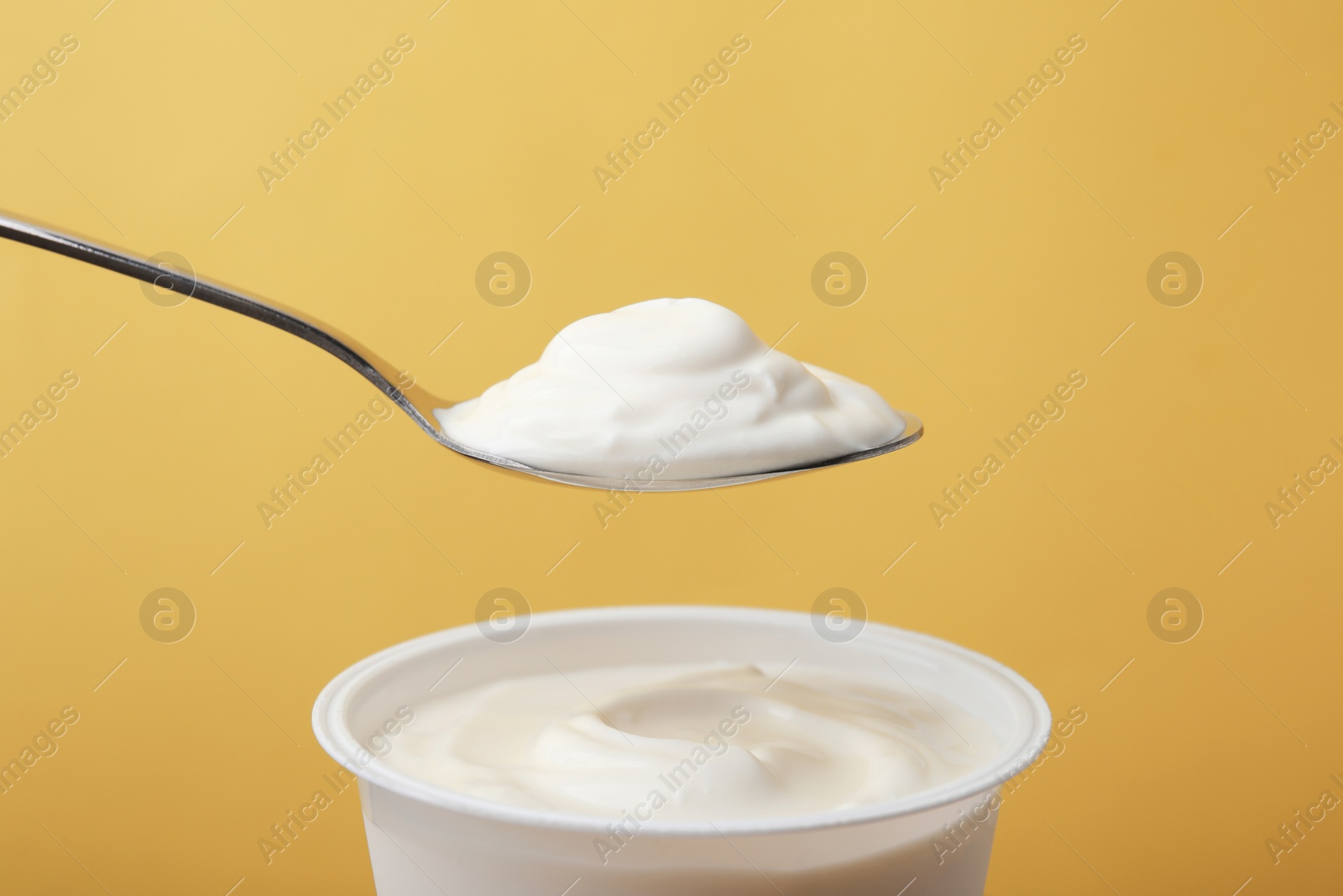 Photo of Eating delicious natural yogurt on yellow background