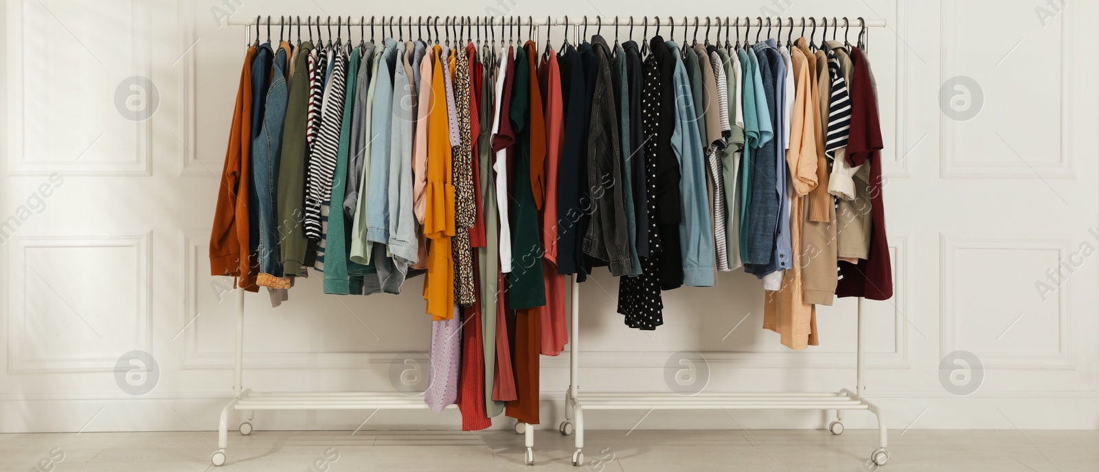 Image of Racks with stylish clothes near white wall indoors, banner design. Fast fashion