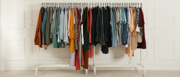 Image of Racks with stylish clothes near white wall indoors, banner design. Fast fashion