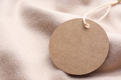 Photo of Circle shaped tag with space for text on beige fabric, closeup