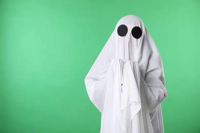 Photo of Creepy ghost. Person covered with white sheet on green background, space for text