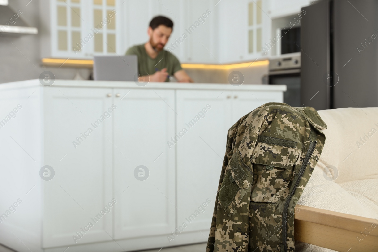 Photo of Soldier using laptop at table in kitchen, focus on uniform. Military service