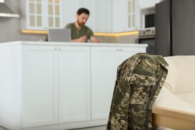 Photo of Soldier using laptop at table in kitchen, focus on uniform. Military service