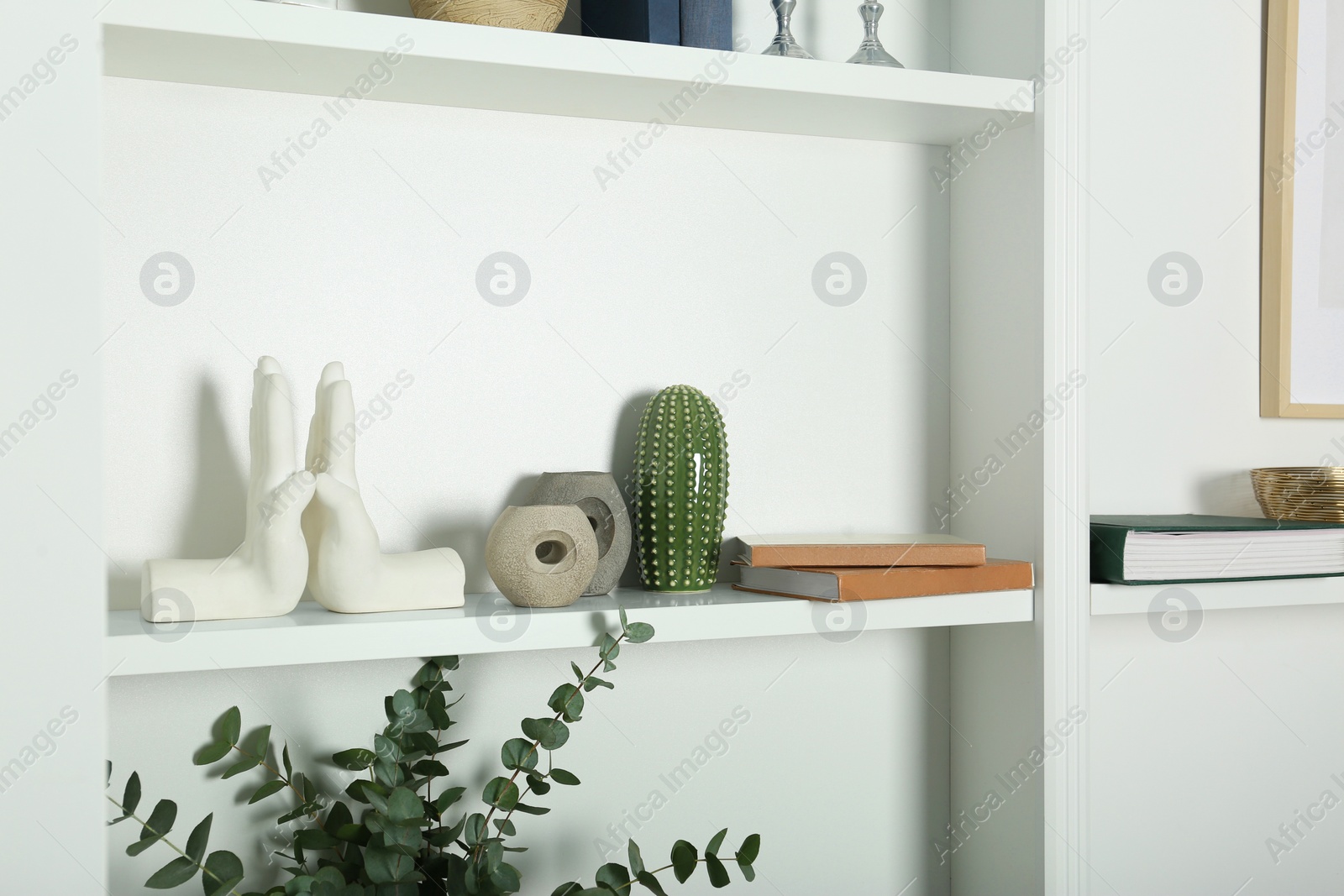 Photo of White shelves with books and different decor indoors. Interior design