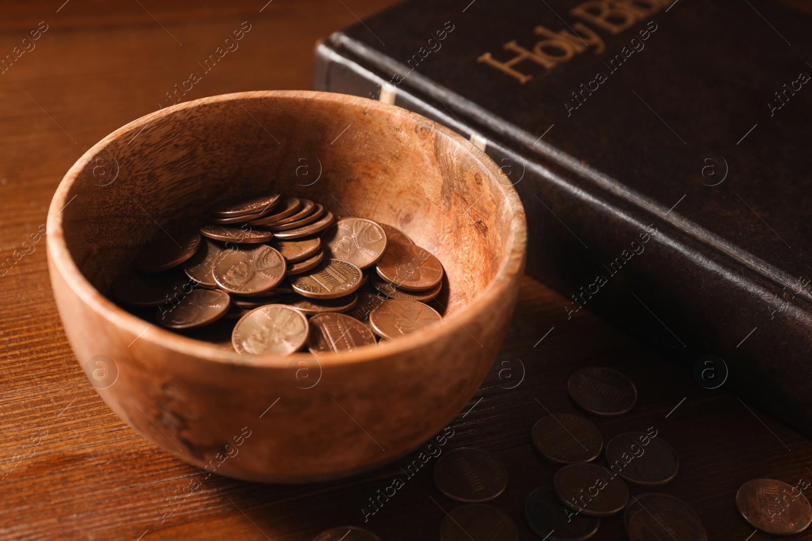 Photo of Donate and give concept. Coins in bowl and Bible on wooden table, closeup