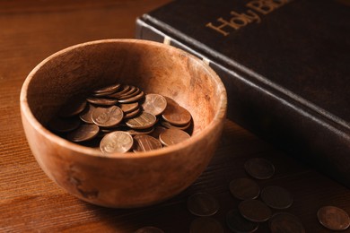 Photo of Donate and give concept. Coins in bowl and Bible on wooden table, closeup