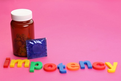 Photo of Word IMPOTENCY, jar of pills and condom on pink background