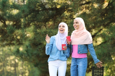 Muslim women with cups of coffee walking in park