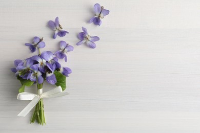 Photo of Beautiful wild violets and space for text on white wooden table, flat lay. Spring flowers