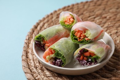 Photo of Plate of different delicious spring rolls wrapped in rice paper on light blue background, closeup