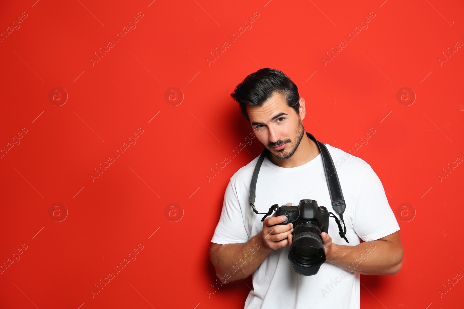 Photo of Young photographer with professional camera on red background. Space for text