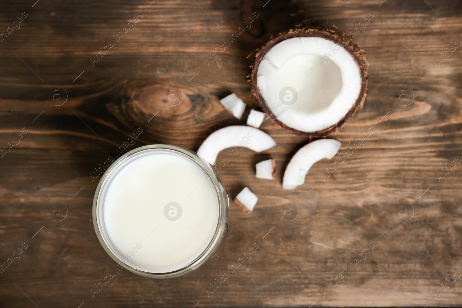 Photo of Glass of coconut milk and fresh nut on wooden background, top view