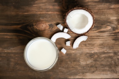 Glass of coconut milk and fresh nut on wooden background, top view