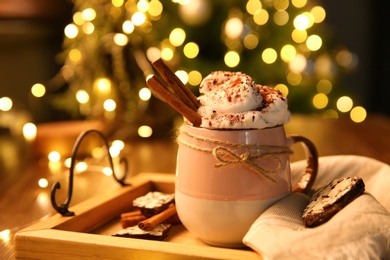 Photo of Tasty hot drink with whipped cream on table against blurred Christmas lights, closeup