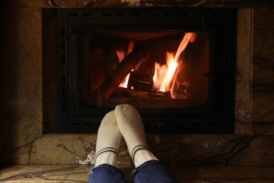 Photo of Woman in warm socks resting near fireplace indoors, closeup